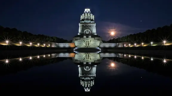 Illuminated monument to the Battle of the Nations with a full moon.