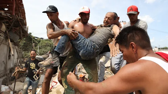 Neighbors carry a man who was rescued from the rubble of a collapsed building after an earthquake in La Guaira, Venezuela.