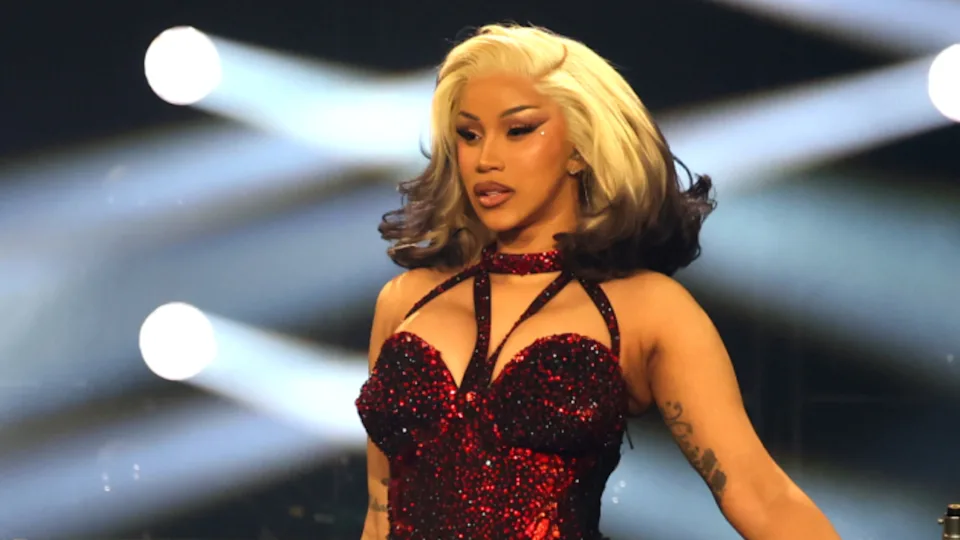 Cardi B performs in a sparkling red outfit with dramatic lighting and a confident pose on stage.