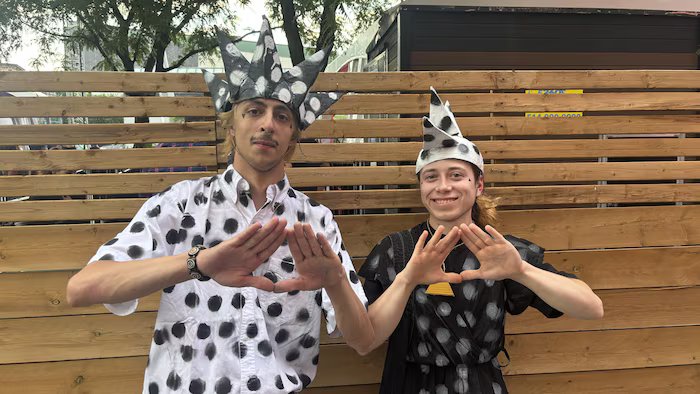 Two people dressed in polka dots form a triangle with their hands. 