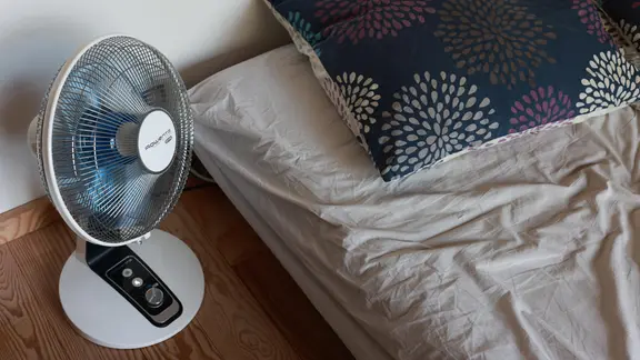 The fan is next to the bed.