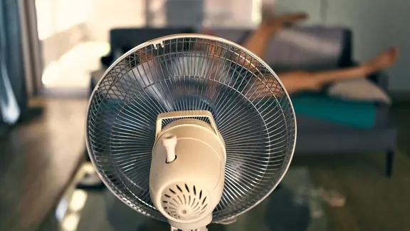 The fan is aimed at a woman lying on the sofa.