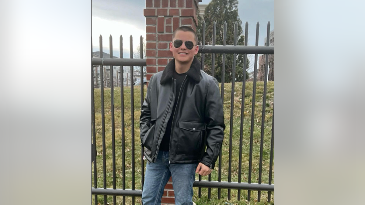 Collin Gosselin smiles in a black jacket, jeans and black sunglasses.