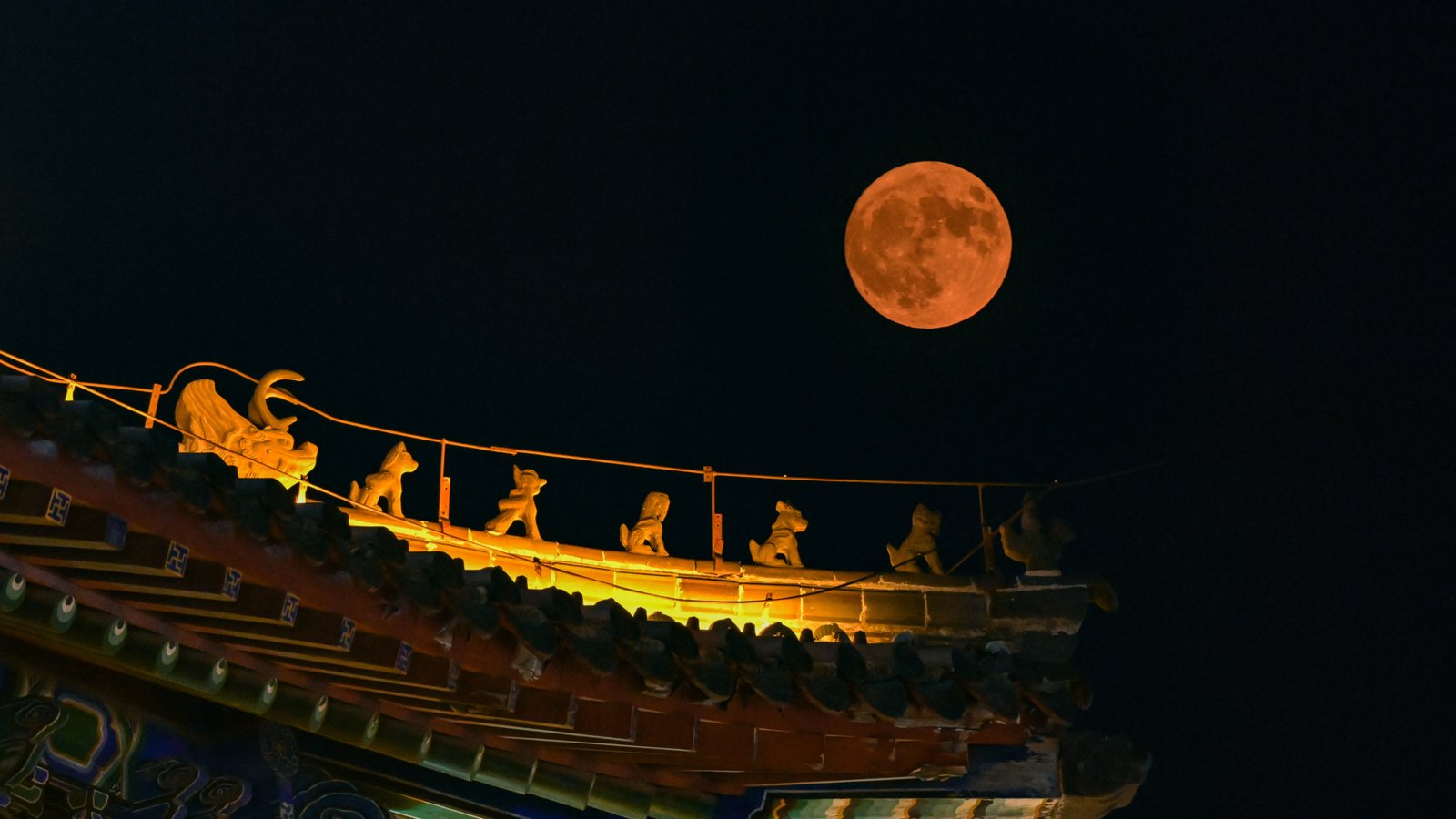 June's Strawberry Moon will be a welcome treat for skywatchers around the world. Here are our favorite photos 27 The full moon shines a rusty orange hue above the ornate roof, adorned with colorful tiles and animal figurines.