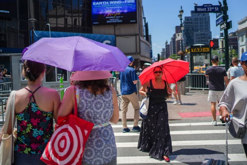 Pedestrians using umbrellas to block the sun cross a street near Madison Square Garden during a heat wave in New York City on Friday, July 3.