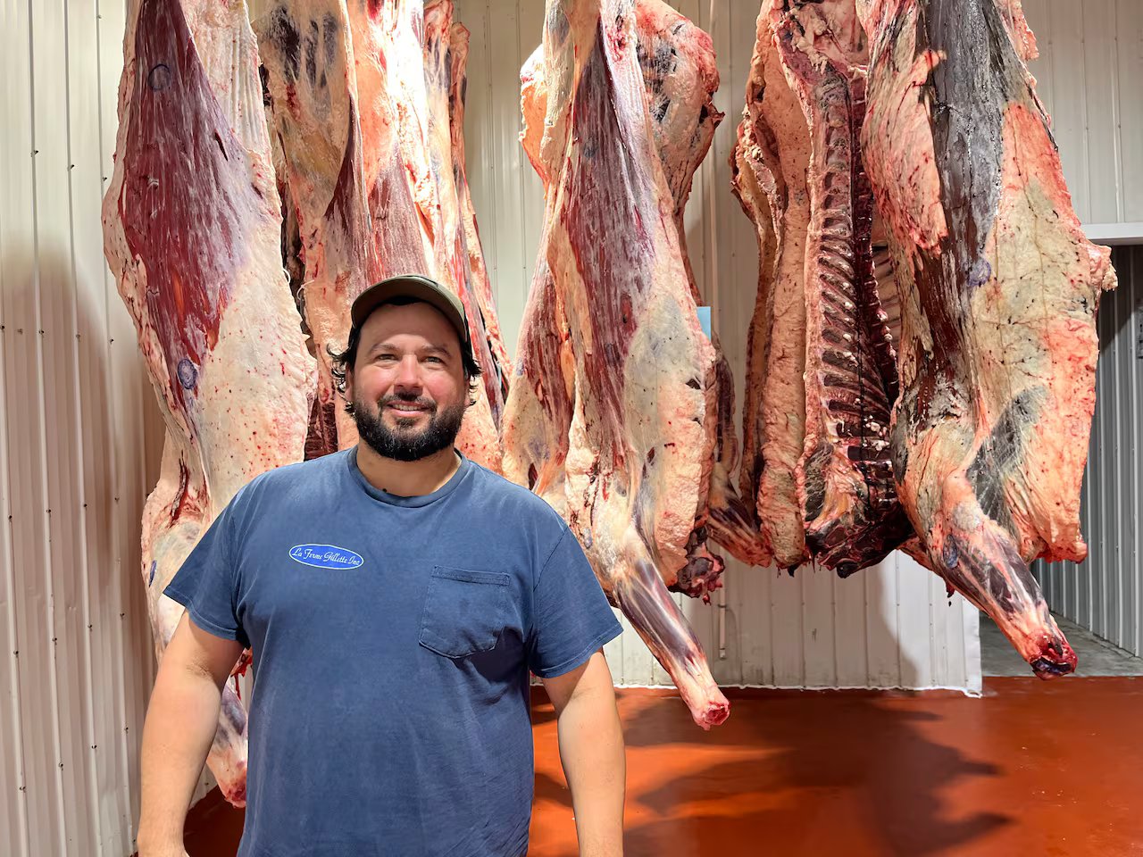 A man stands in front of meat on hooks