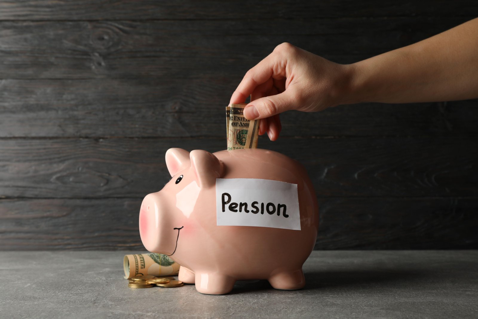 Woman putting money into piggy bank on wooden background