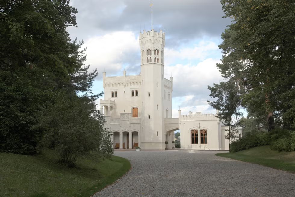 White castle with a high tower surrounded by trees and cloudy sky.
