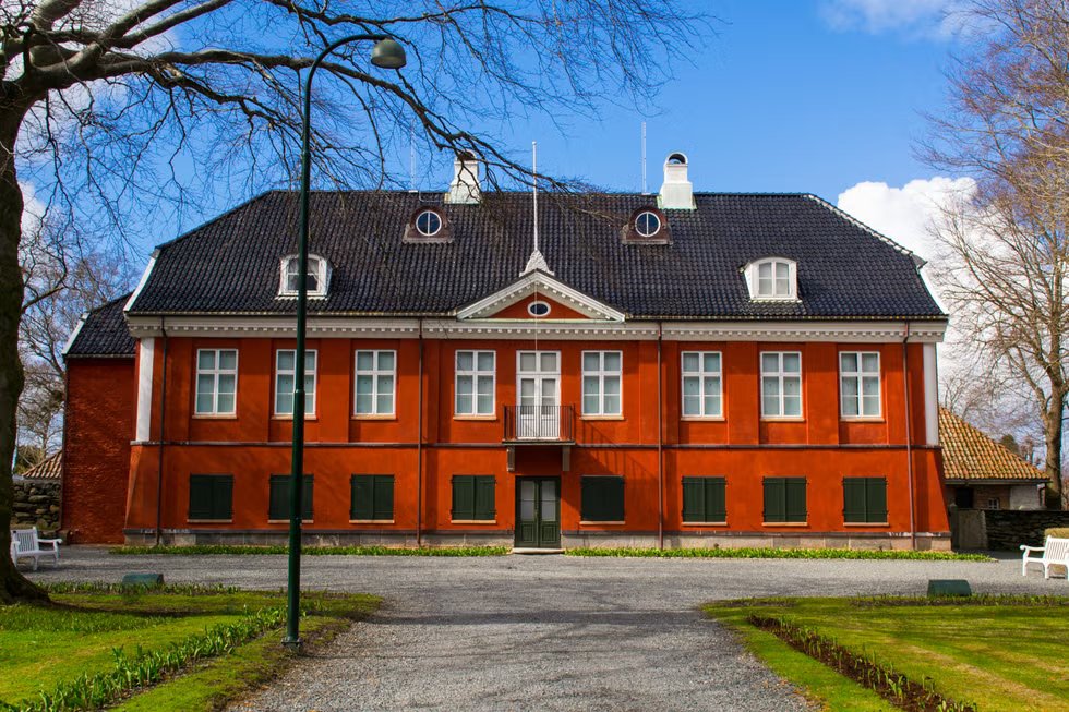A historic red brick building with dormer windows and a small balcony against a blue sky.