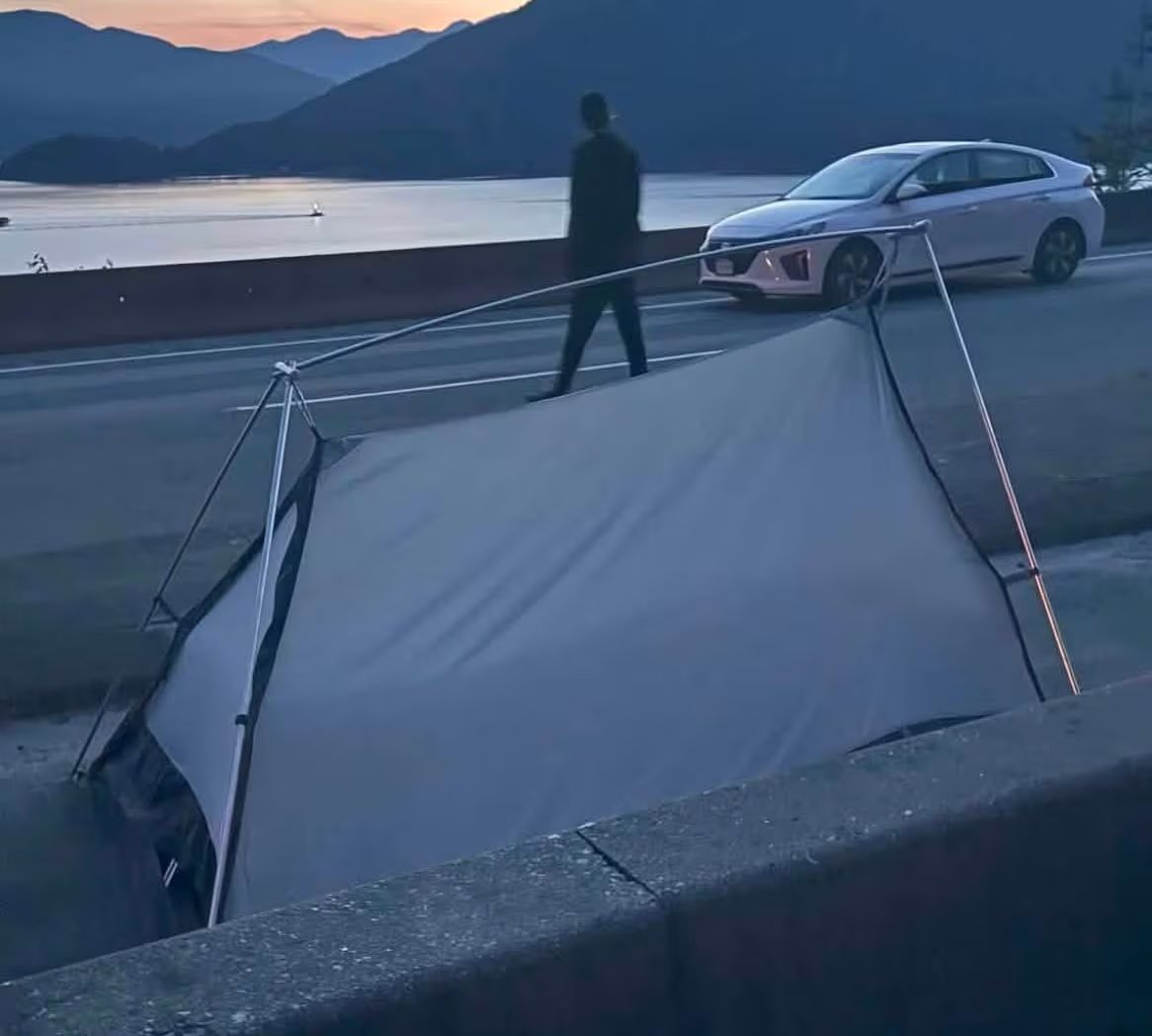 A tent erected on the roadway, behind which there is a parked car and a person walking behind it.