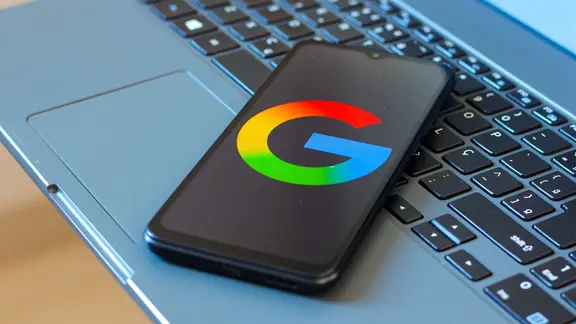 A cell phone lies on the laptop keyboard. The Google logo appears on the display.