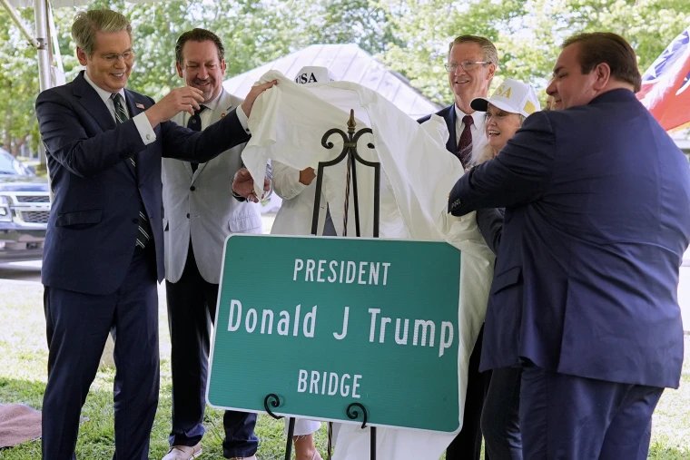 Scott Bessent and other officials remove a white sheet from a green road sign that reads 