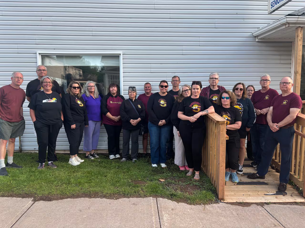 A group of people stands in front of a blue building.