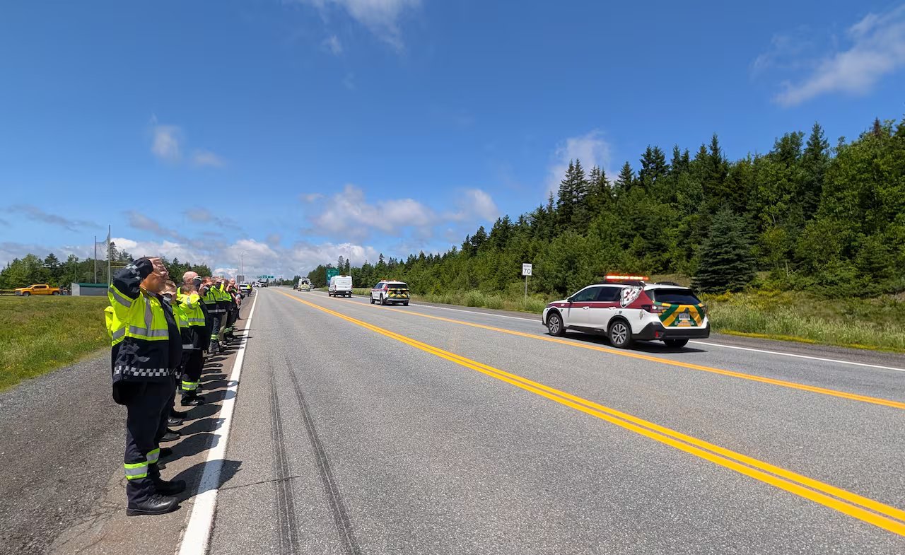 First responders stand along the side of the road and raise their hands to their heads in salute.