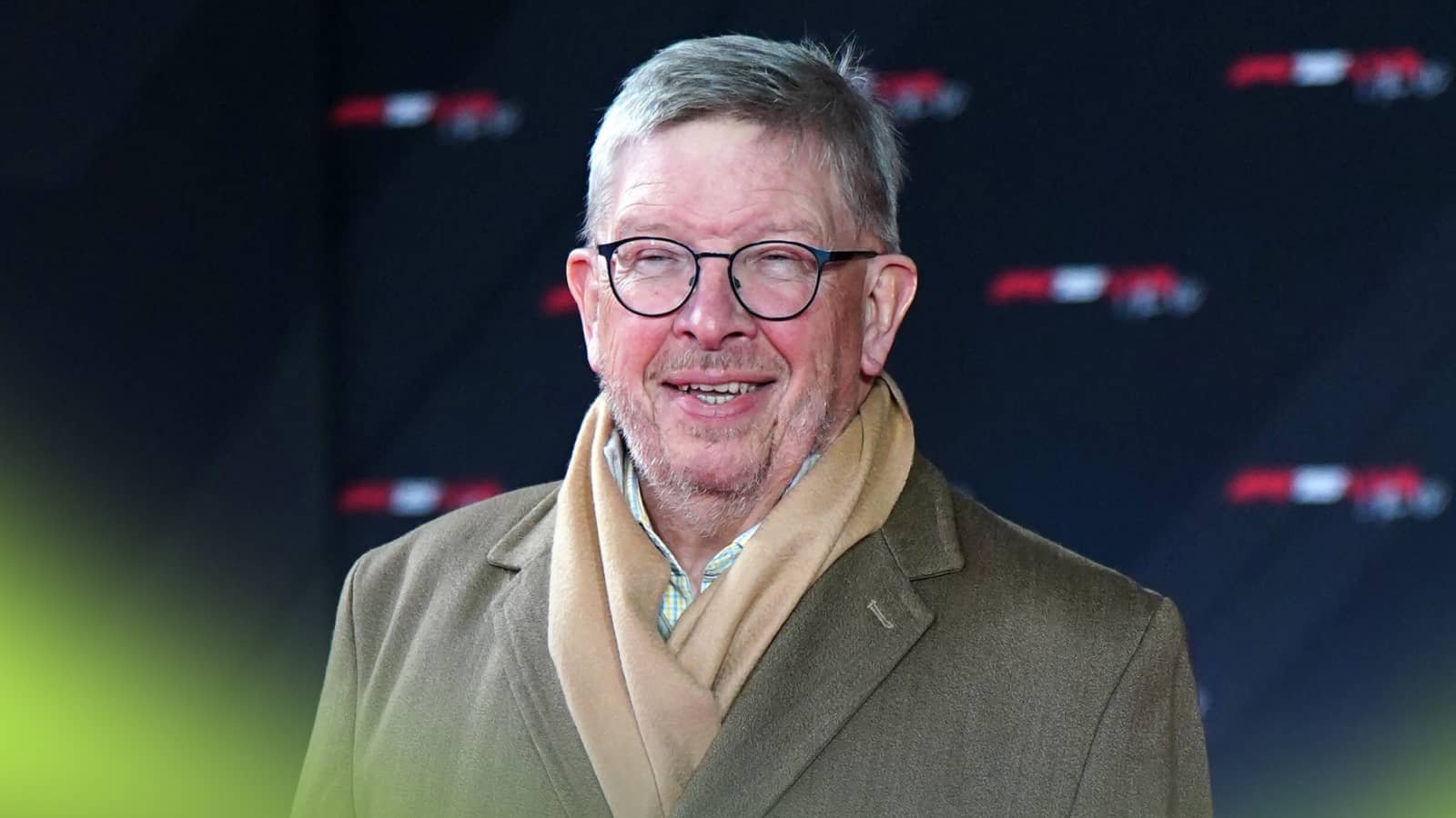 Ross Brawn smiles widely in a coat and scarf.