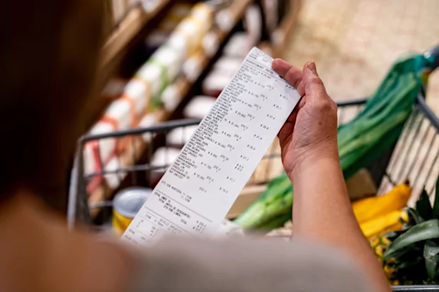 Close-up of woman looking at receipt after shopping at supermarket - cost of living concepts