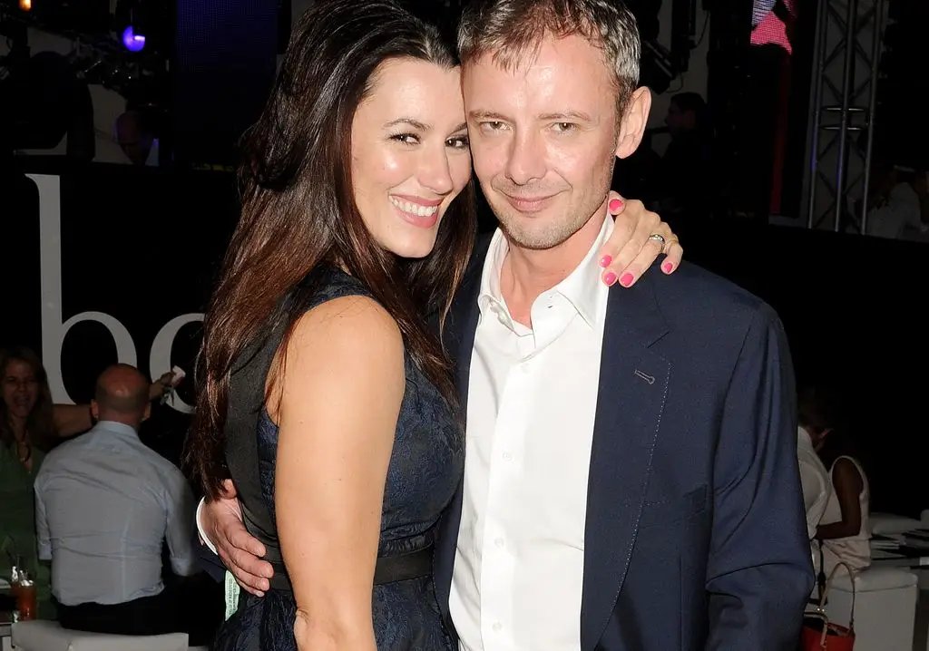 John Simm in a blue suit and white shirt hugs his wife Kate in a dress
