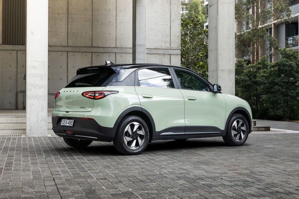 Light green Geely EX2 SUV, rear view from a three-quarter angle, parked on a paved area near concrete columns.