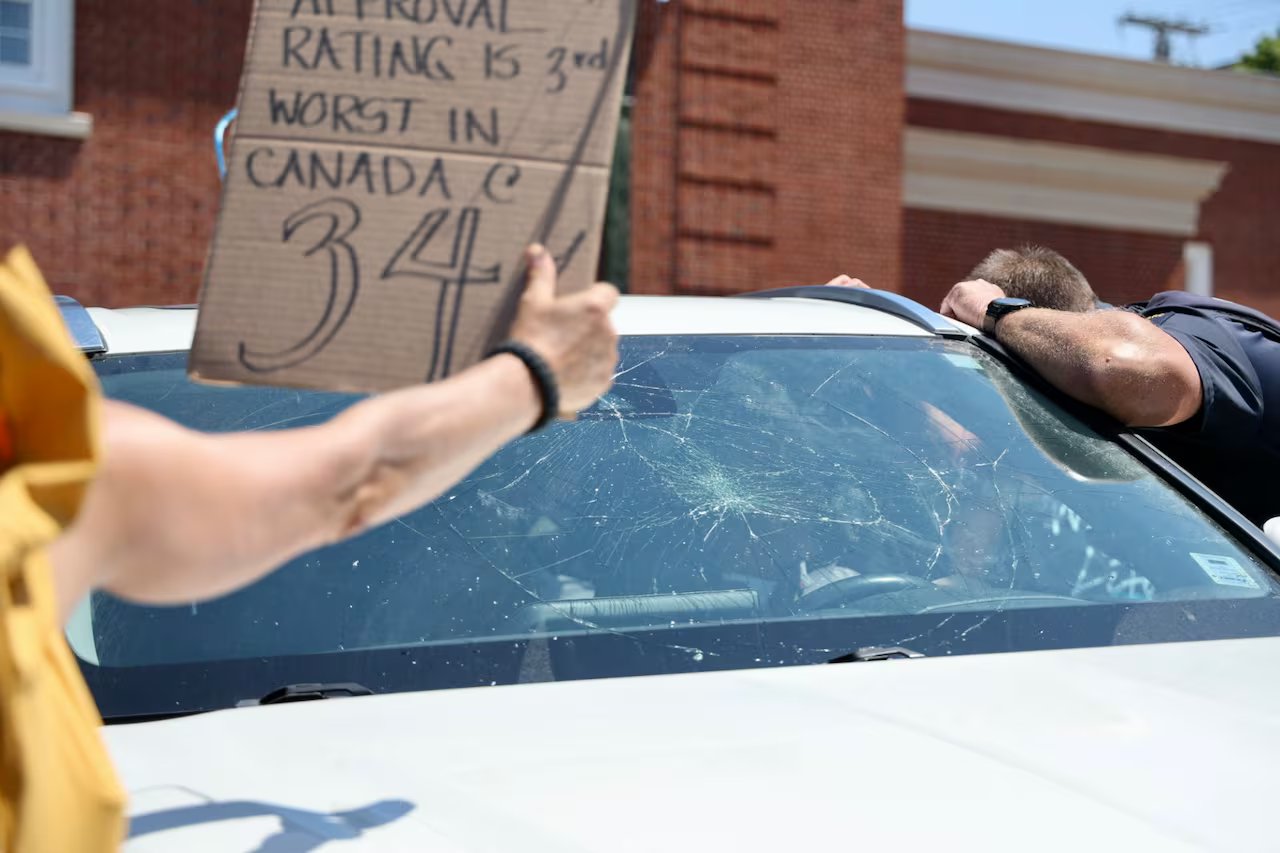 man holding cardboard sign in front of broken windshield