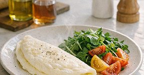 A plate of soft white omelette accompanied by arugula and tomato salad.