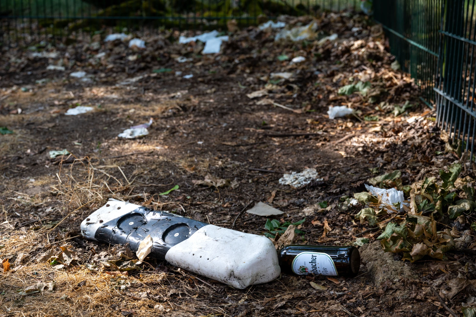 Dirt accumulates on the green area fence: a broken guide post, a beer bottle, feces and numerous napkins.