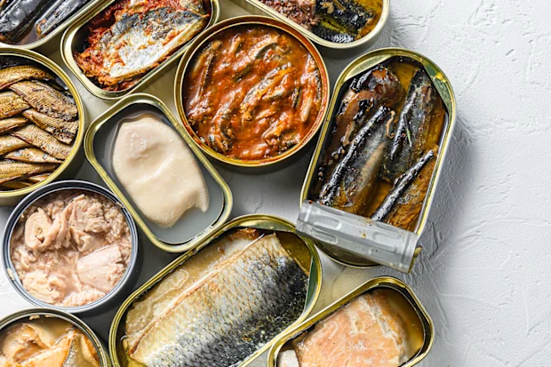 Sardine shortage: With sardines missing from shelves, what are the best canned fish? 27 In tin cans for canned food products, saury, mackerel, sprats, sardines, sardines, squid, pineapple, tuna, corn, peas, mango, beans are preserved, on a white textured background with space for text on top.