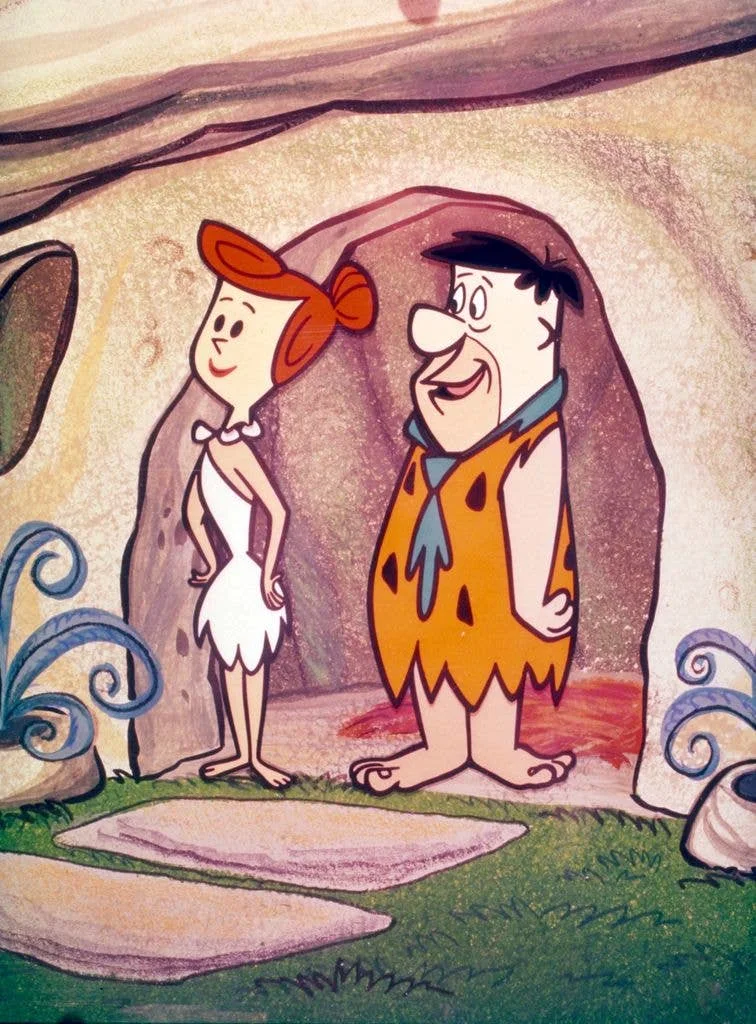 Wilma and Fred Flintstones stand in the doorway of their cave.