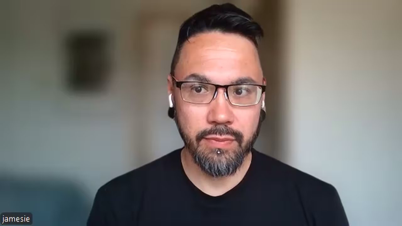 A man in glasses and a black T-shirt with headphones.
