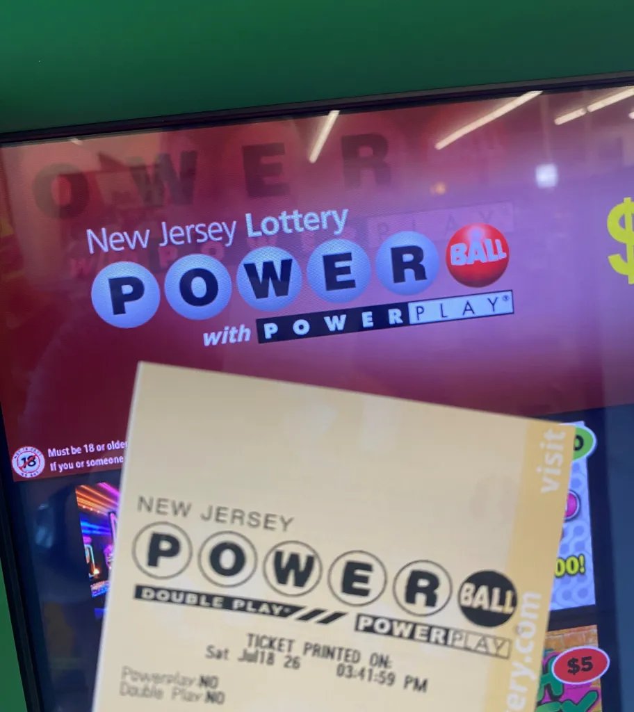 A Powerball lottery ticket in front of a digital screen with the New Jersey Powerball logo.