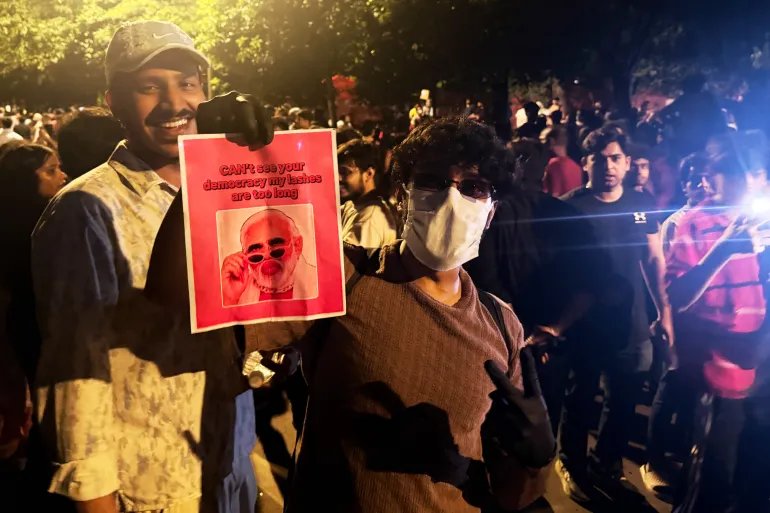 A protester holds a poster with a portrait of Prime Minister Narendra Modi and text. 