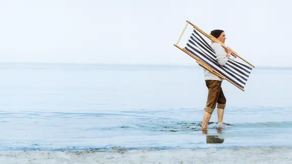 A man walks on the water with a folded deck chair on his shoulder.