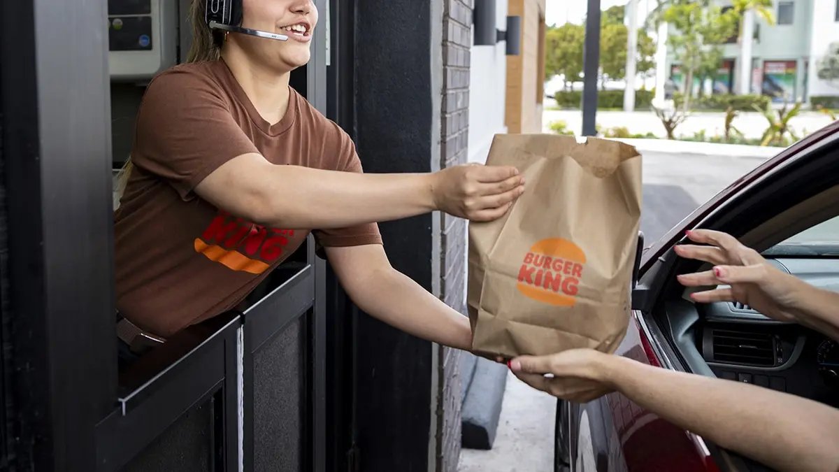 A Burger King employee hands a bag of food to a customer at a gas station.