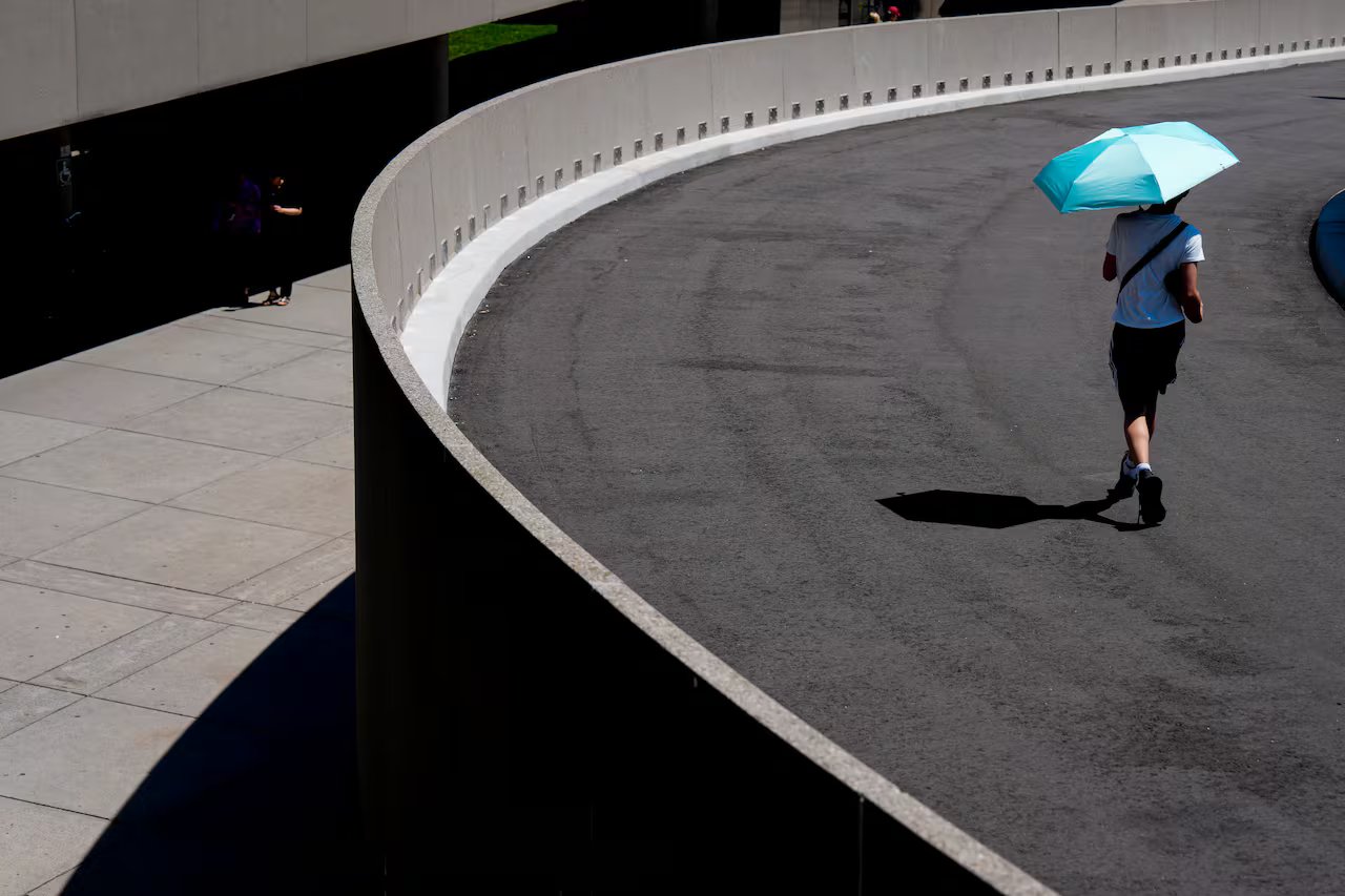 A man on a hill running along a concrete path under an umbrella on a sunny day.