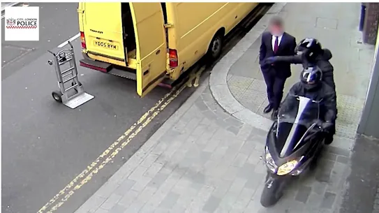 A thief steals a mobile phone from a man walking down a London street.