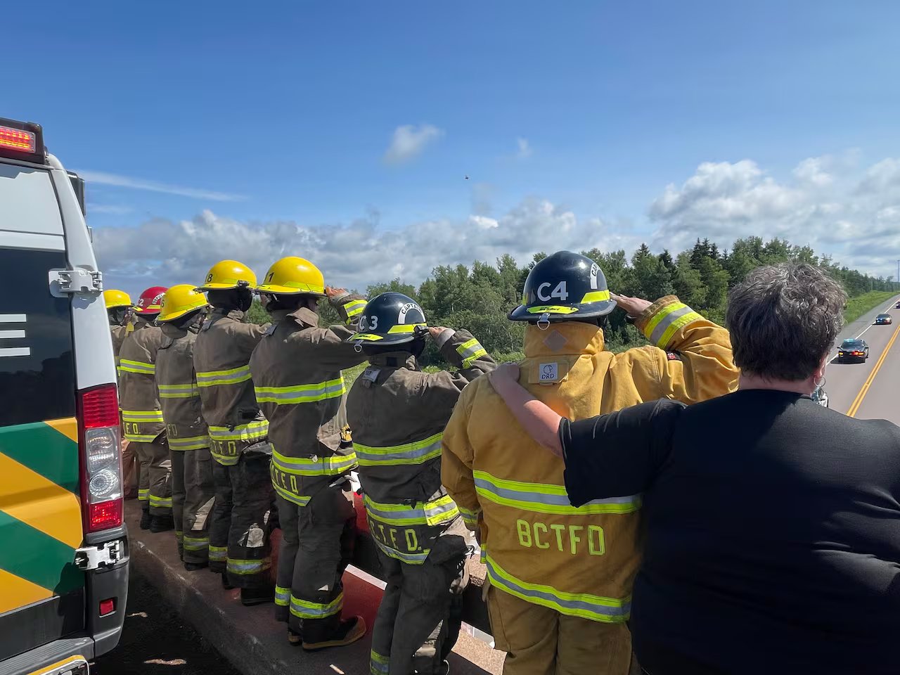 Several firefighters on the overpass greet PEI paramedics Mike McKenzie and Jenna Croucher as the procession taking them home to the island passes underneath it on the Trans-Canada Highway near Bayfield, North Carolina.