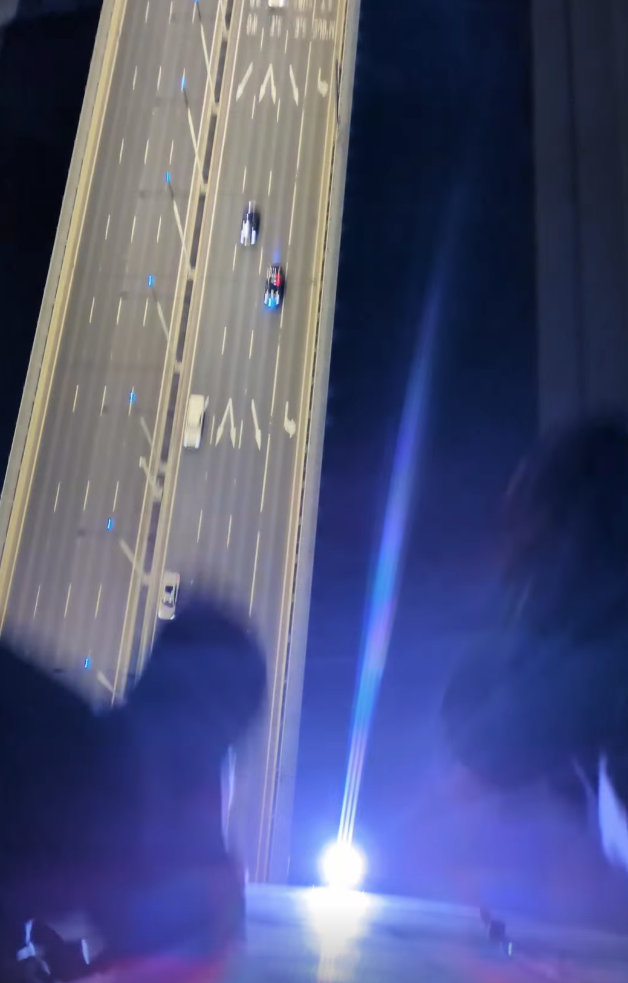 Police confront graffiti vandal Pam Bird on Bolt Bridge 14 Two black shoes hang in the air high above the roadway, cars pass below.