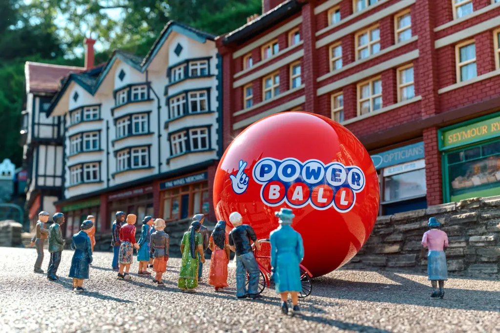 Miniature figures standing in front of a giant red Powerball in a model village.