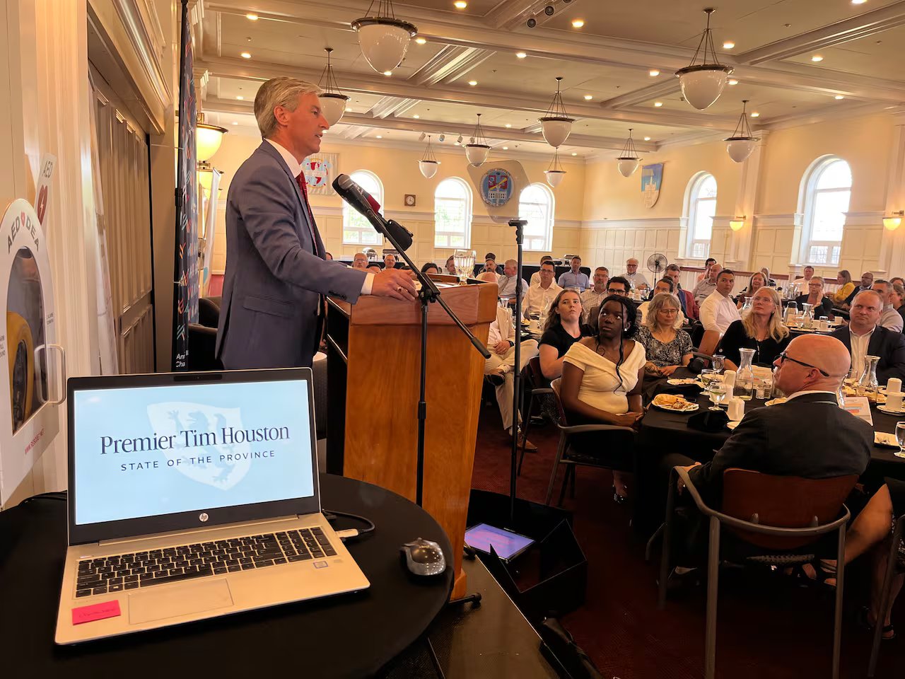 A man on a podium is talking to a room full of people sitting at tables.