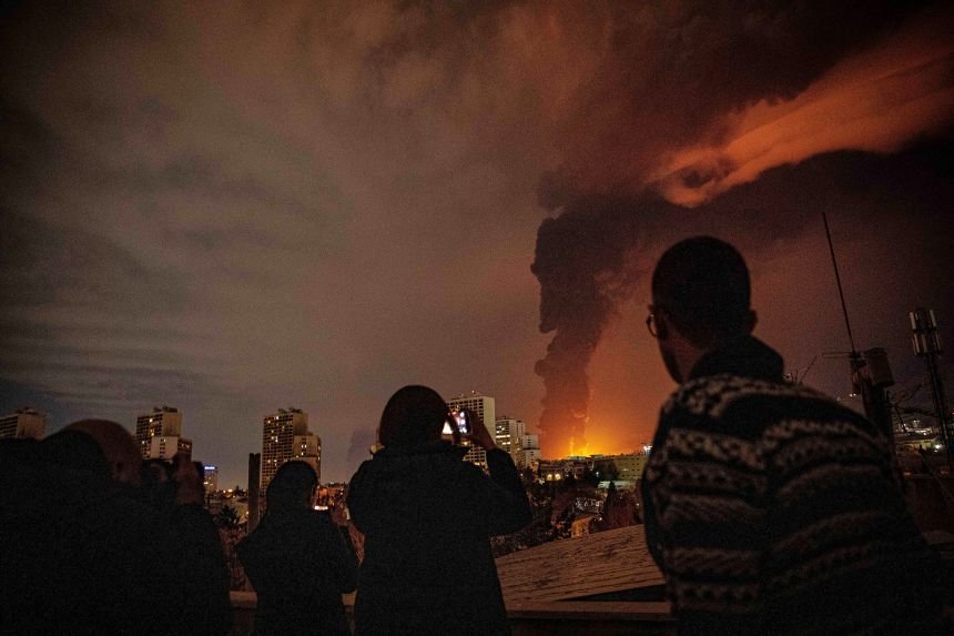 Residents watch and photograph as flames and smoke rise from an oil storage facility in Tehran, Iran, which was damaged after the March 7 US-Israeli attack.