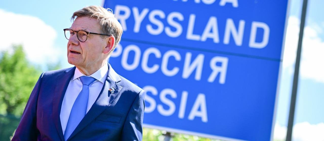 Johann Wadeful stands on the Finnish-Russian border in front of a sign with inscriptions in several languages. 