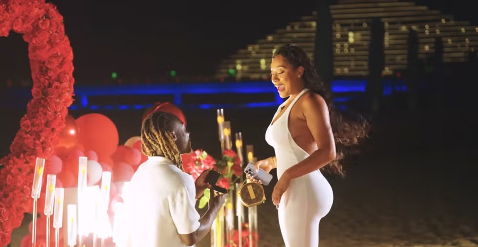 Romantic beach proposal surrounded by roses and balloons at night.