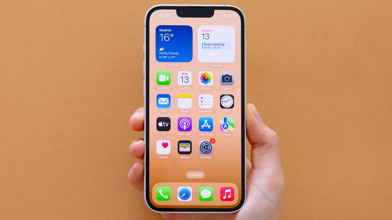 Hand holding iPhone 16E on beige background