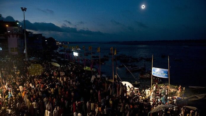 Thousands of people are gathered to watch a solar eclipse in the dark sky above.